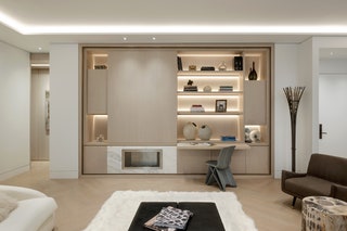 pull out beige desk under welllit builtin shelving gray chair white rug brown chair in foreground