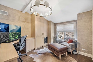 beige walls white chandelier plaid chair and leather ottoman to left under window lshaped desk with large monitor black...