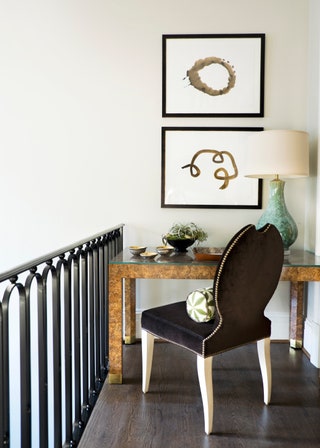 glass topped desk pulled up to wall on landing beneath two vertically stacked framed abstract artworks black iron...