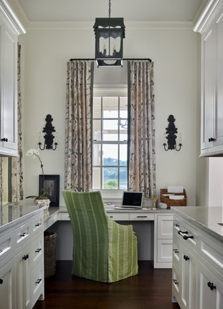 long curtains over a tail window flanked by two black candle sconces black pendant light hanging overhead green chair...