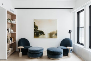 two matching blue cushioned chairs with round blue ottomans angled toward each other two round matching side tables...