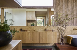 Bathroom with skylight overhead soaking tub to right floating cabinet storage beneath sink mirror round black planter in...