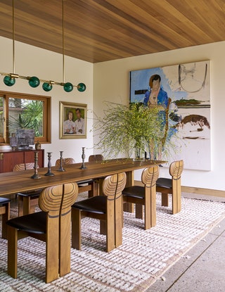 Dining room with long wooden table surrounded by chairs wood plank ceilings light fixture above table with round green...