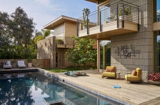 Rectangular inground swimming pool to left balcony with plants overlooking pool deck to right yellow and orange chairs...