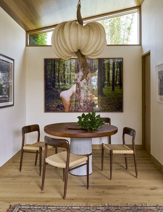 Dining area with slanted ceiling overhead from which a large light sculpture hands over a round table which is...