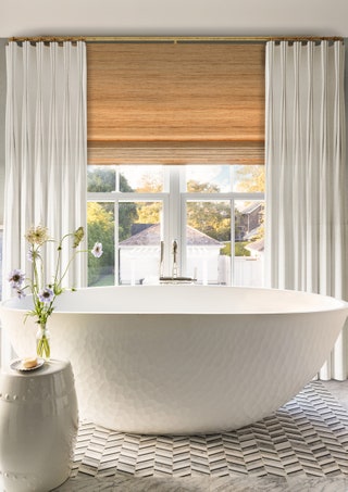 In the primary bathroom a view of the pool and poolhouse beyond is framed by window treatments from The Shade Store. A...