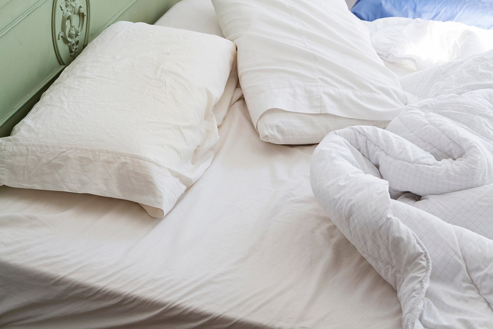 unmade bed with white bedding pale green headboard