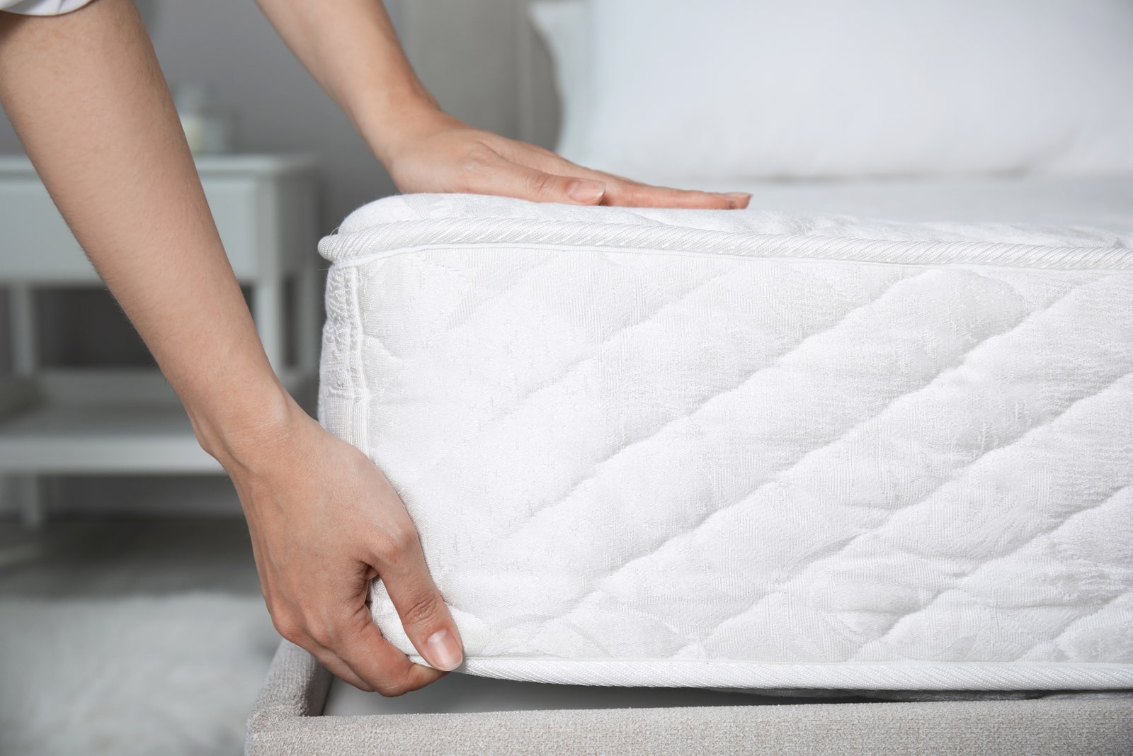 Woman putting soft white mattress on bed indoors closeup